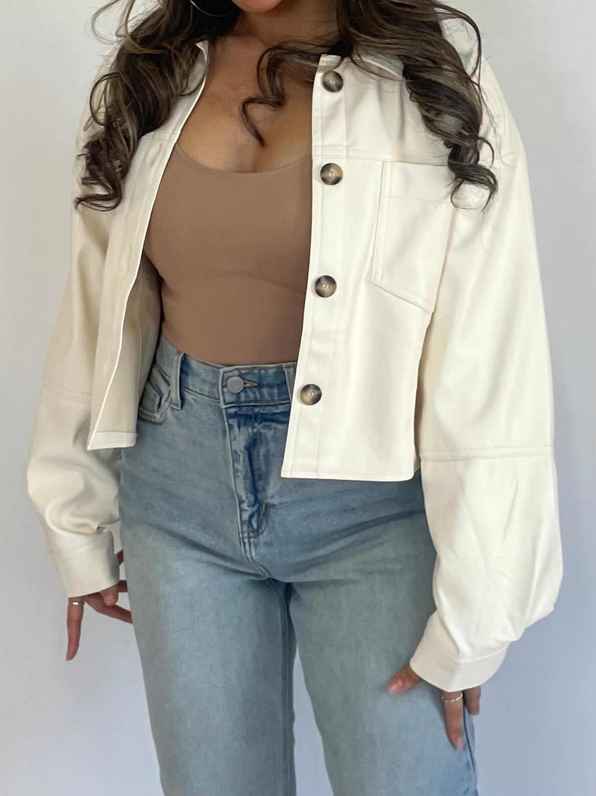 This ivory leather jacket is made from vegan leather and features a cropped, button-up design. Its sleek and edgy appearance makes it a versatile piece that can be paired with any outfit!