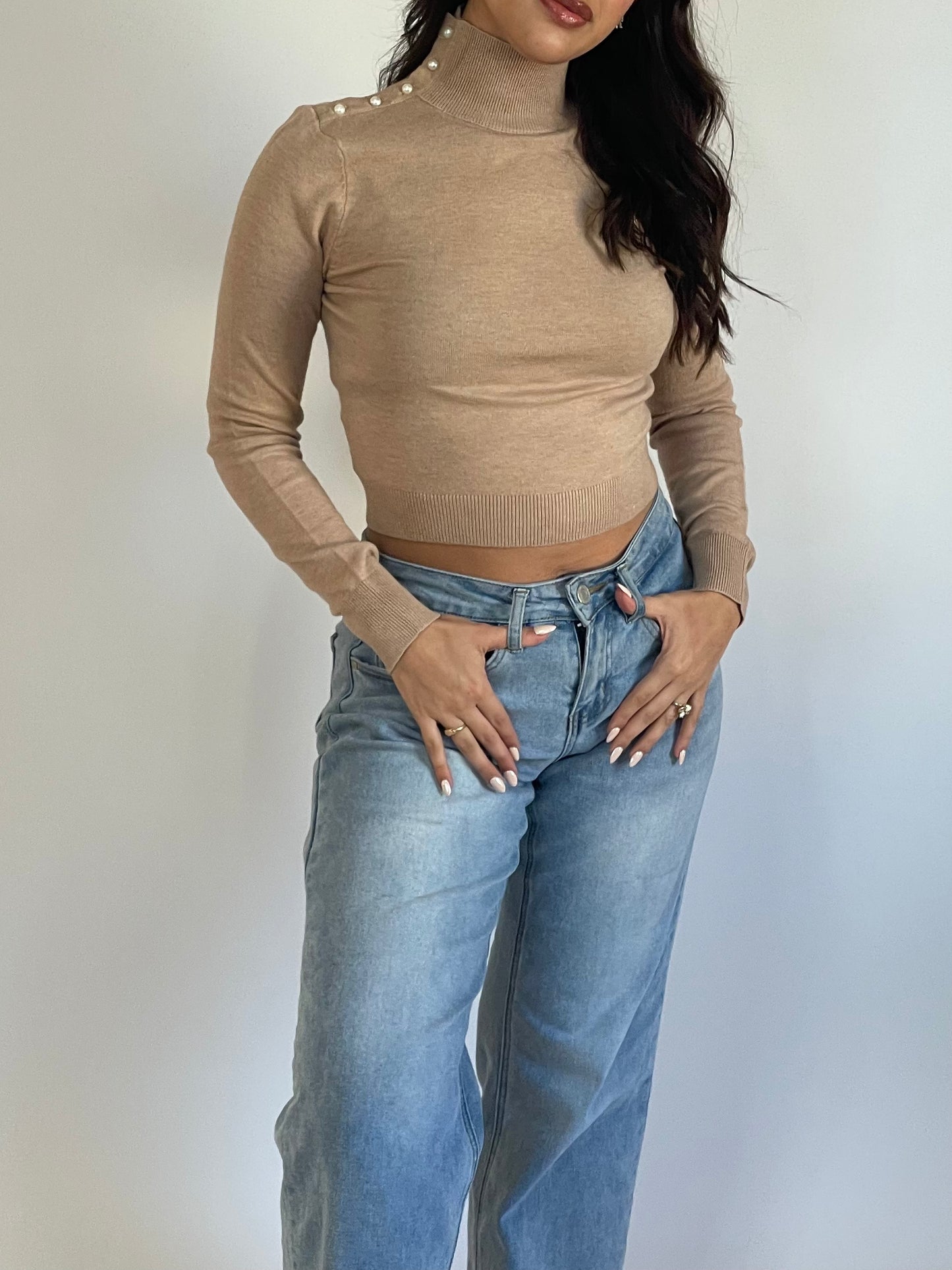 Long sleeve, turtleneck top available in tan or black. Soft, knitted material and a fitted look. Has pearl accents along one side of the neck. 